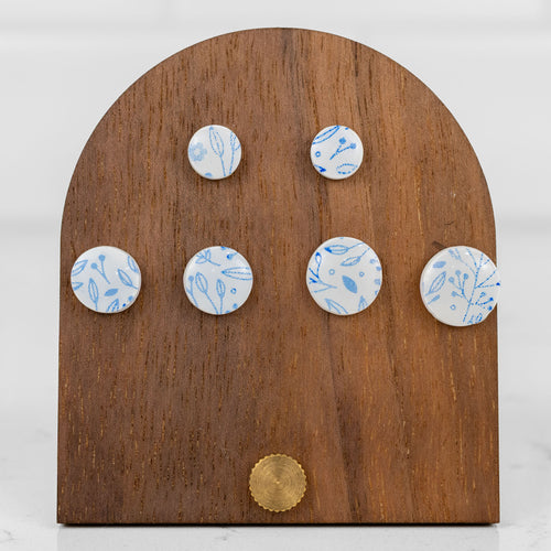 Round white handmade polymer clay stud earrings with a delicate blue floral pattern, shown in three sizes