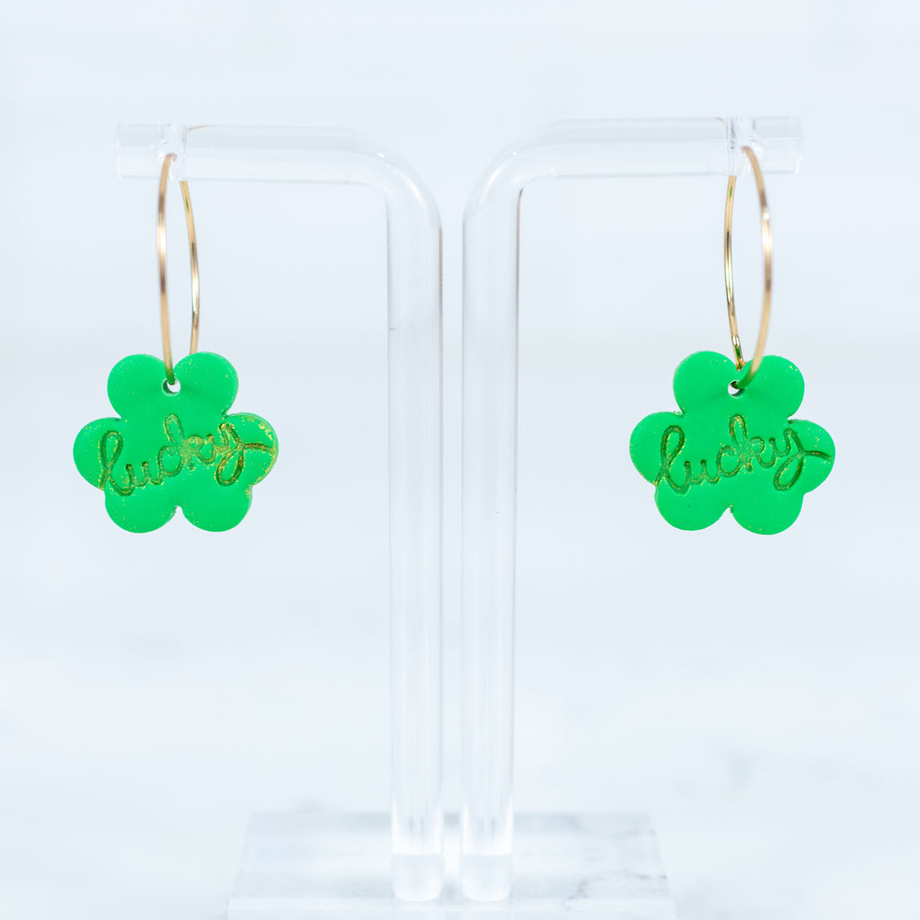 Green clover-shaped earrings with 'lucky' text on a clear background