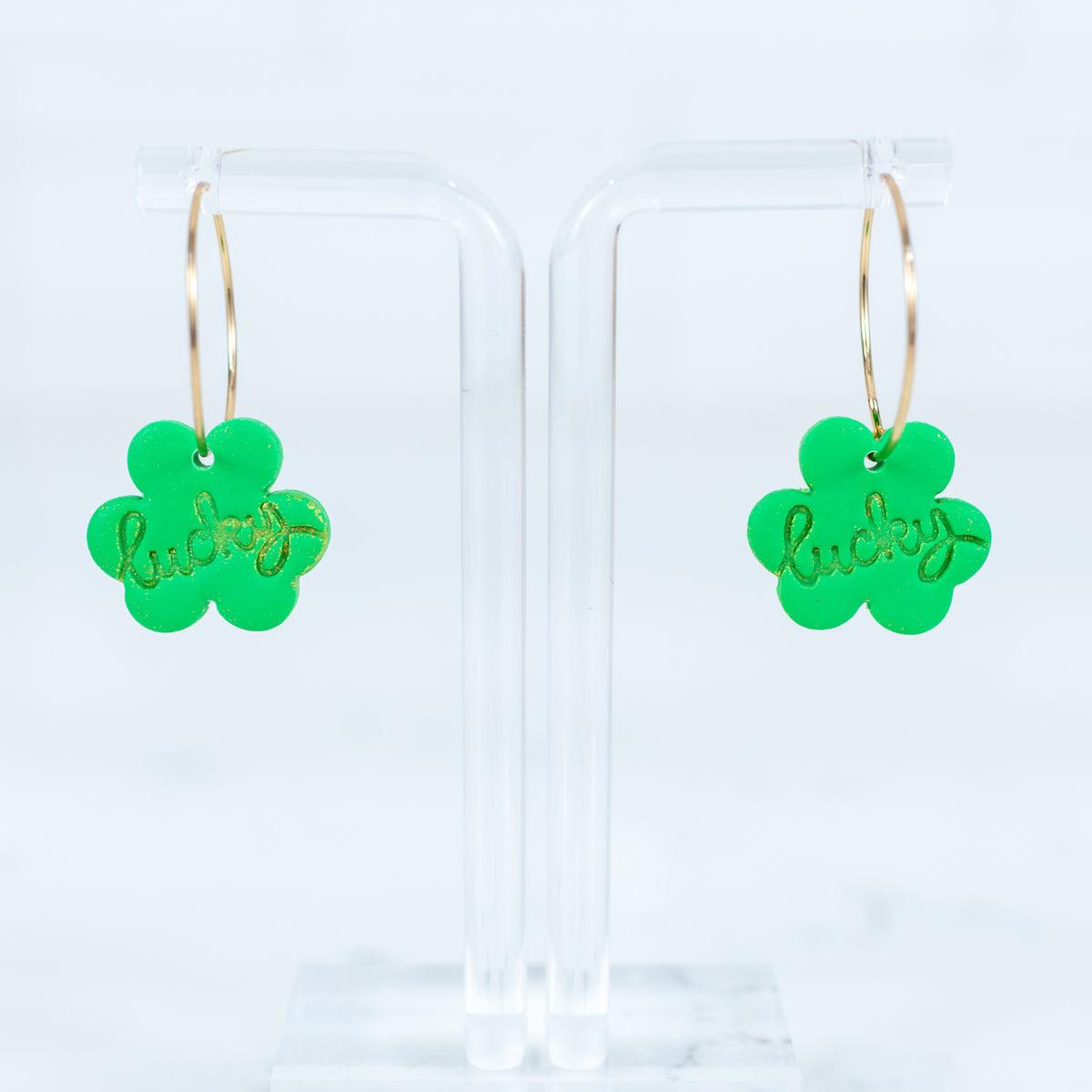Green clover-shaped earrings with 'lucky' text on a clear background