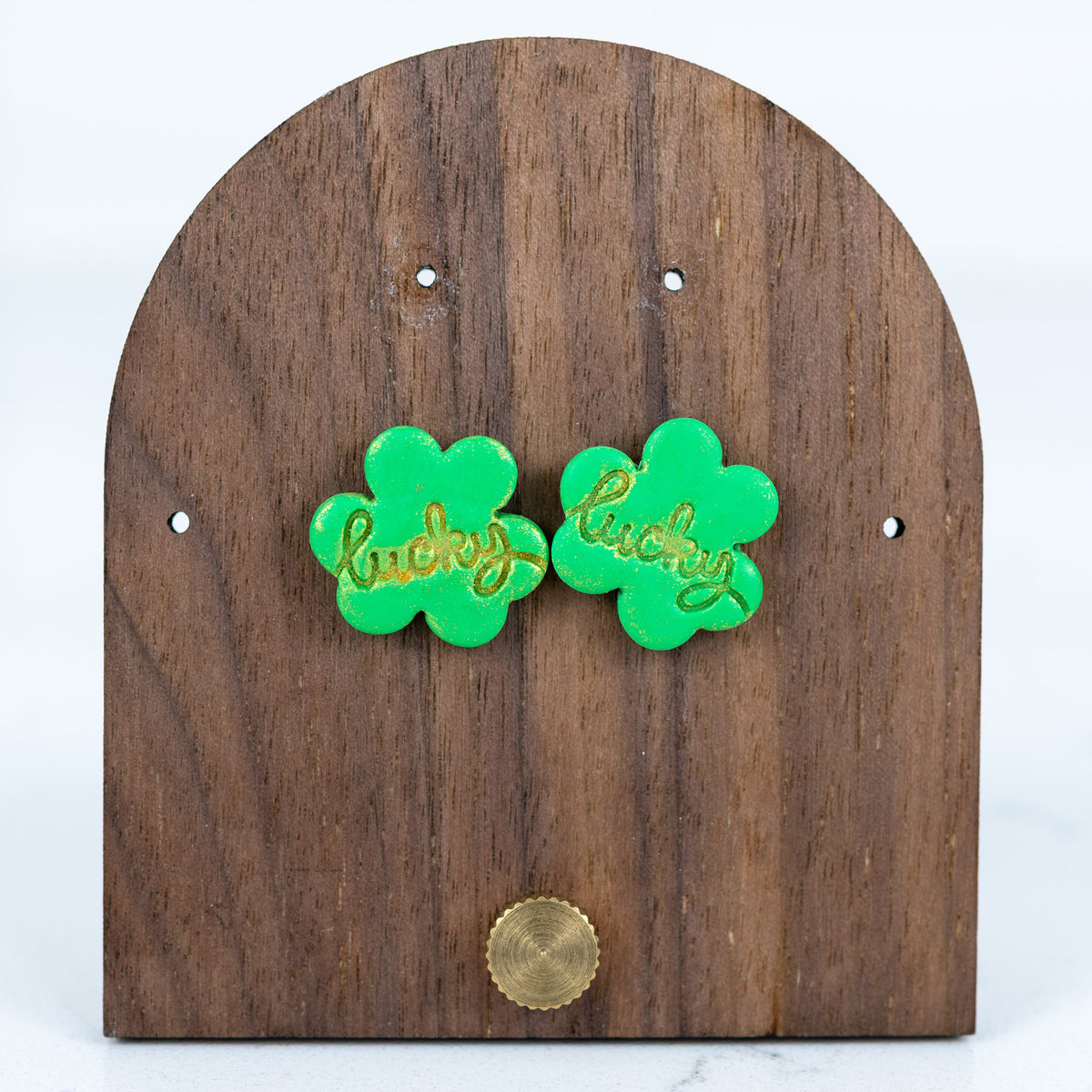 Green clover-shaped earrings with 'lucky' text on a wooden stand.