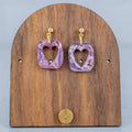 Purple heart-shaped earrings on a wooden display stand with a gray background