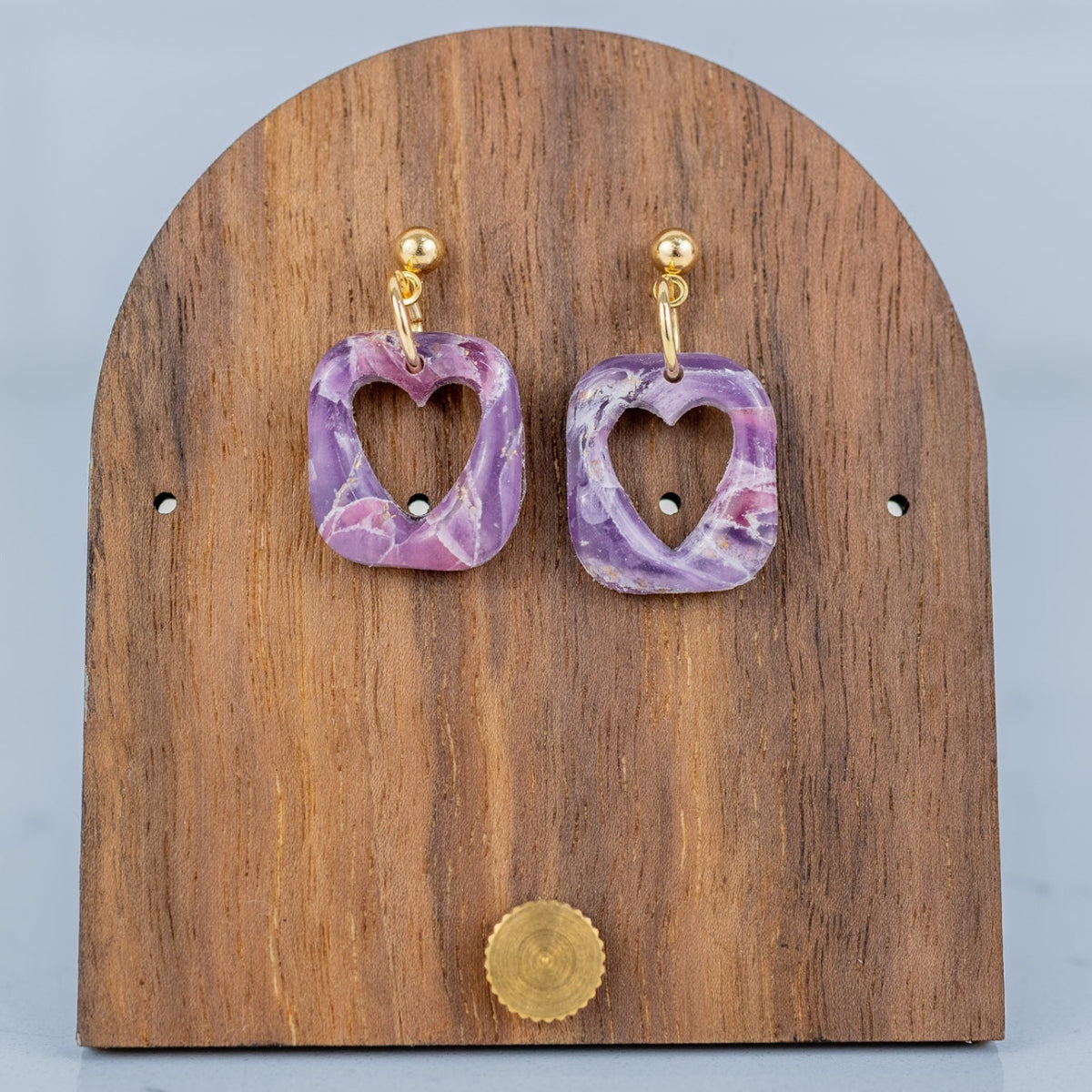 Purple heart-shaped earrings on a wooden display stand with a gray background