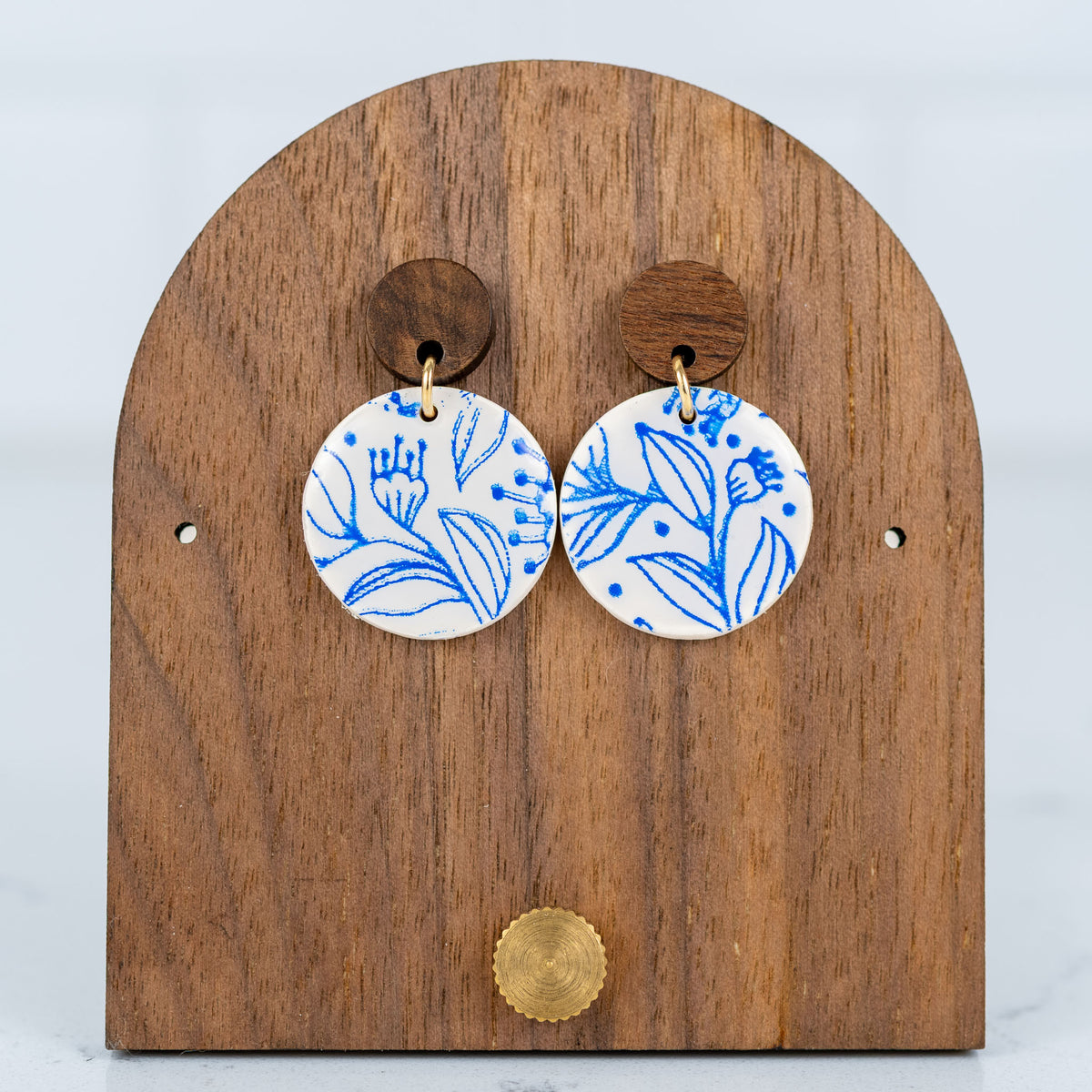 White and blue floral polymer clay circle stud earrings displayed on a wooden earring stand