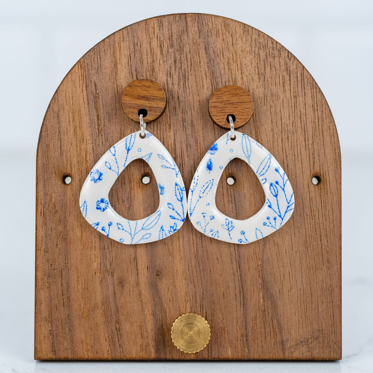 White and blue floral cutout polymer clay dangle earrings displayed on a wooden earring stand