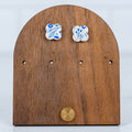 Small white and blue floral polymer clay stud earrings displayed on a wooden earring stand