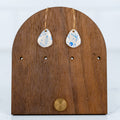 Teardrop-shaped earrings with blue floral design on a wooden earring stand.