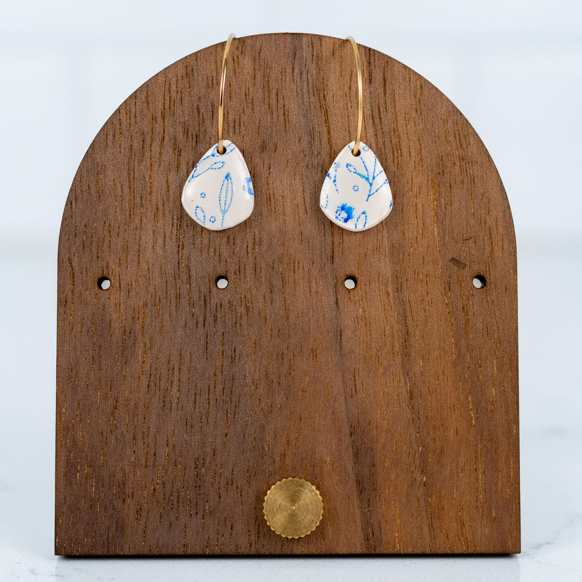 Teardrop-shaped earrings with blue floral design on a wooden earring stand.